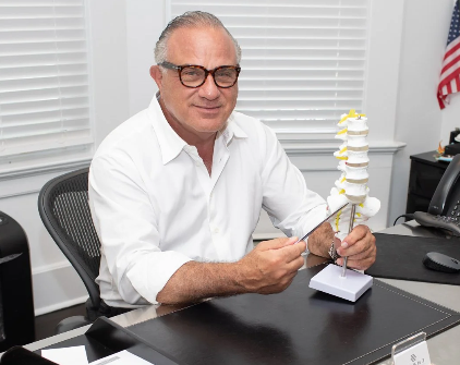 Dr. Jerald P. Vizzone at his desk holding a spine model